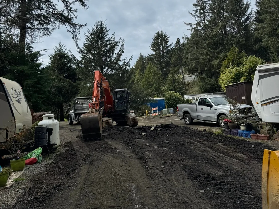 Excavator tearing up an old road surface beside parked trailers, demolition