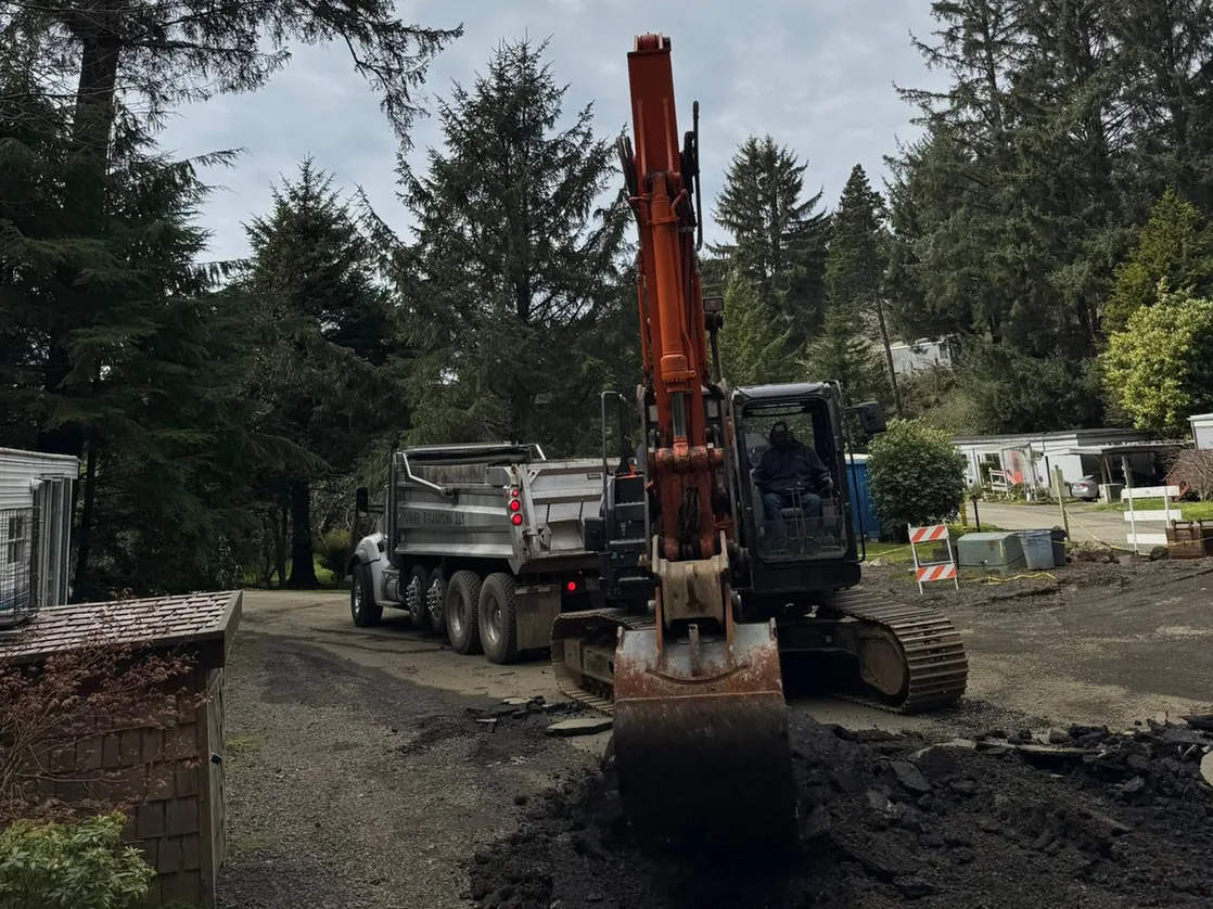Excavator digging out old asphalt with a dump truck behind, demolition