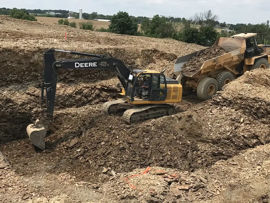 Excavator digging a deep foundation hole beside a dump truck, foundation excavation