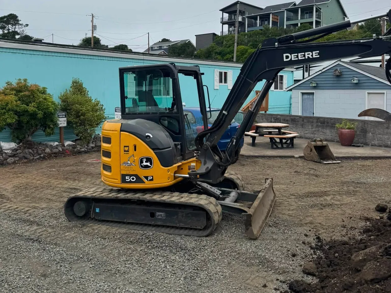 Compact excavator on a gravel lot beside a pile of dug soil, trenching