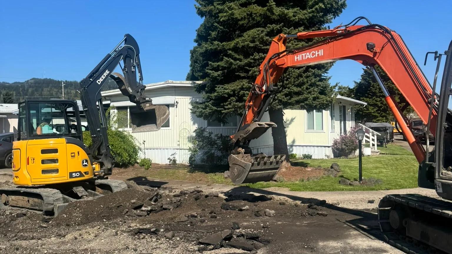 Two excavators digging up old asphalt on a work site, excavation contractor