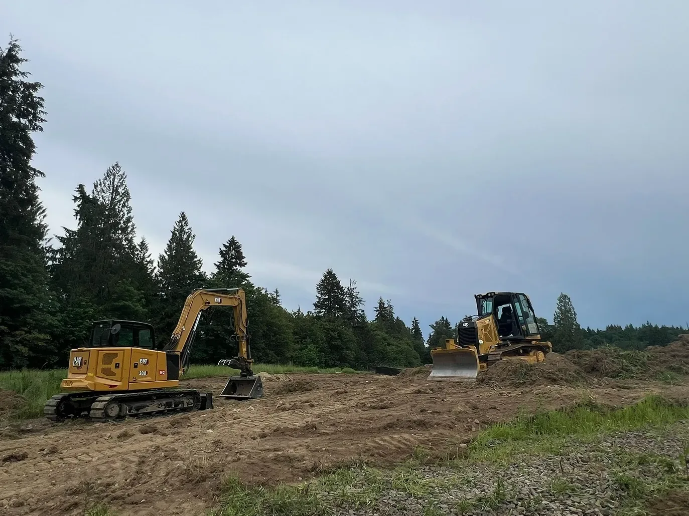 Compact excavator and small dozer rough grading a stripped lot, site preparation