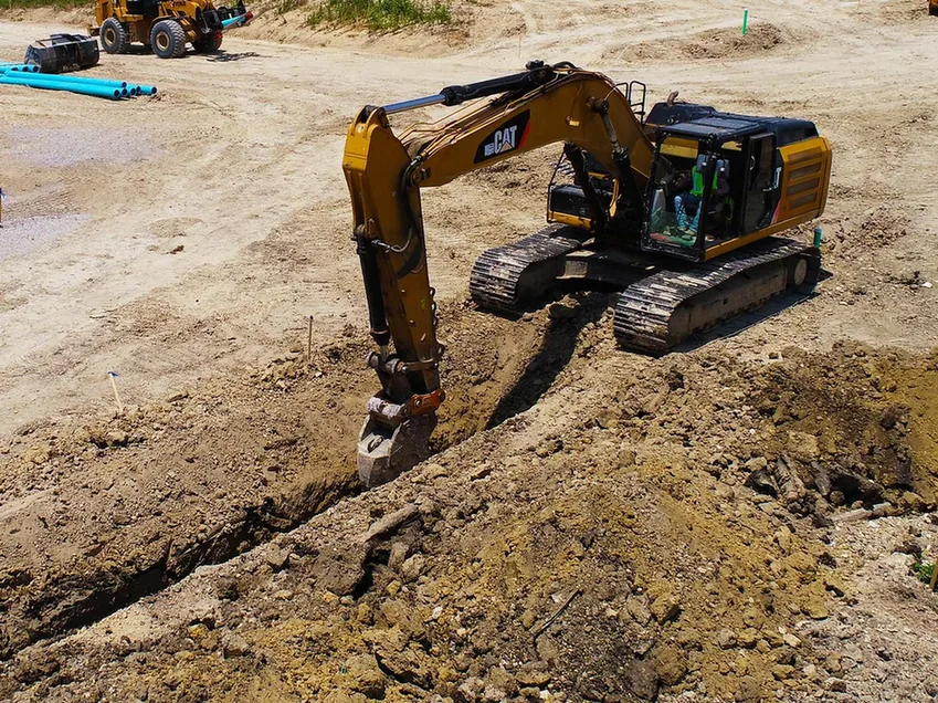 Excavator digging a utility trench on a graded site, subdivision development