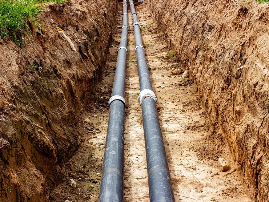 Two black pipes laid along the floor of a long open trench, storm drainage