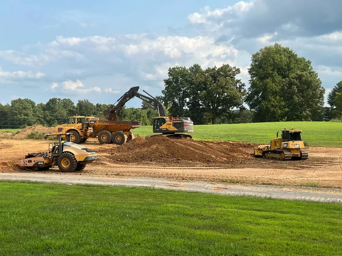 Excavator loading a dump truck beside a dozer and roller, grading earthwork