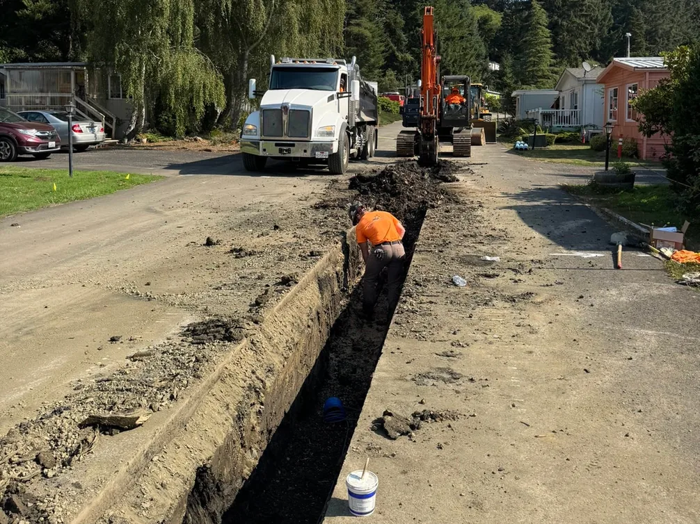 Long open trench along a road with an excavator and dump truck, trenching