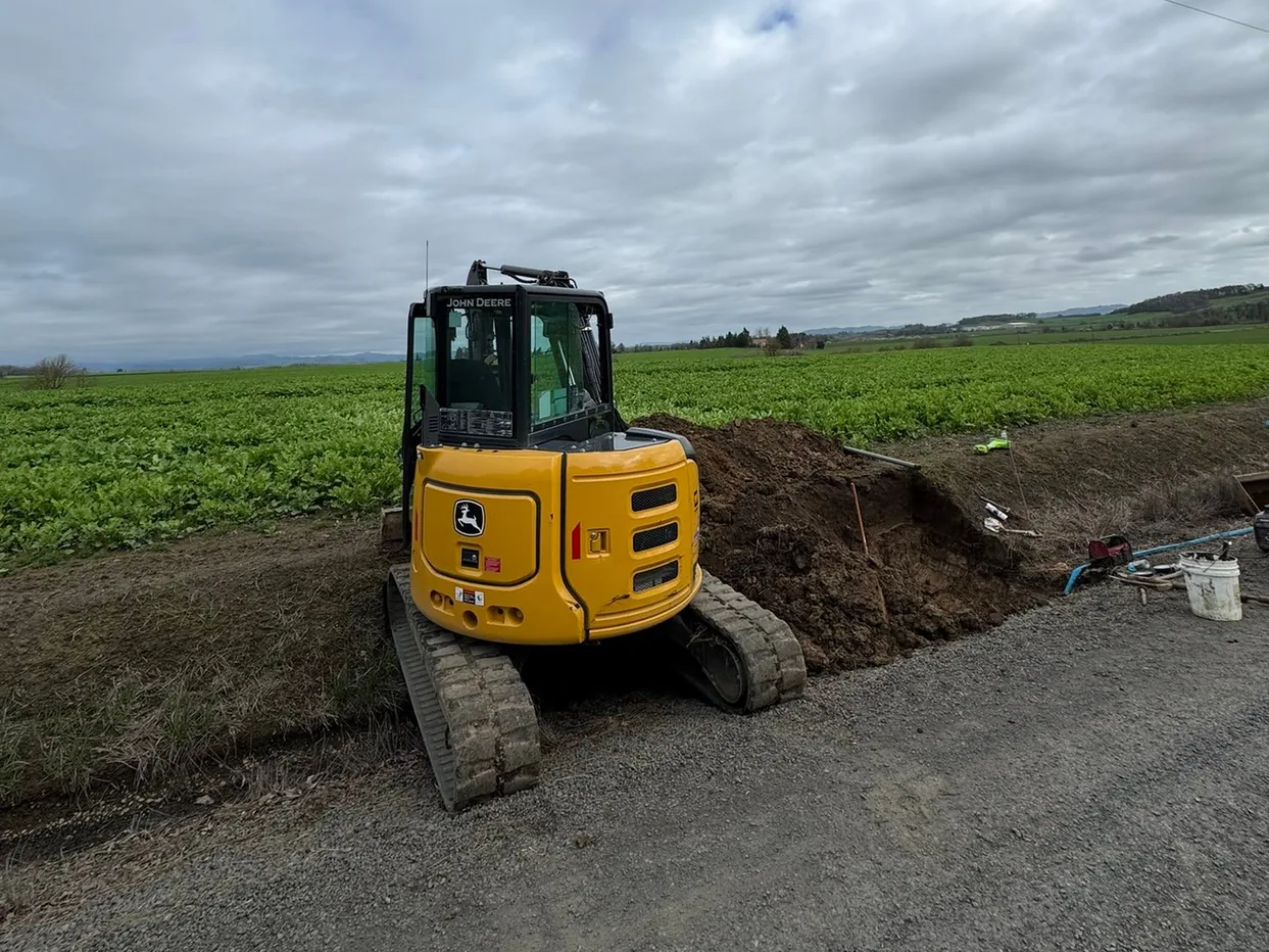Compact excavator beside a fresh trench along a gravel road edge, trenching