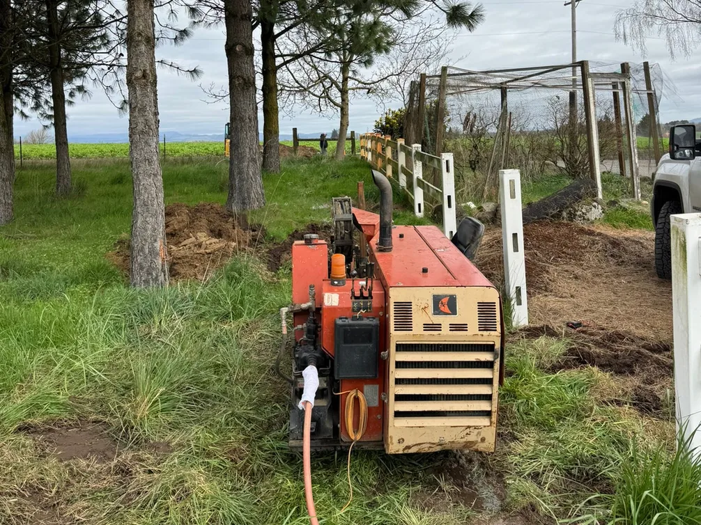 Directional drill rig set up on grass beside a fence, underground utilities