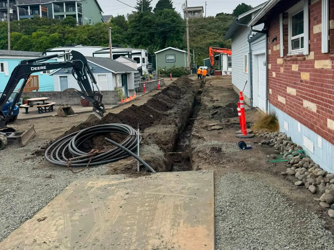 Open utility trench with a coil of black water pipe and an excavator, underground utilities