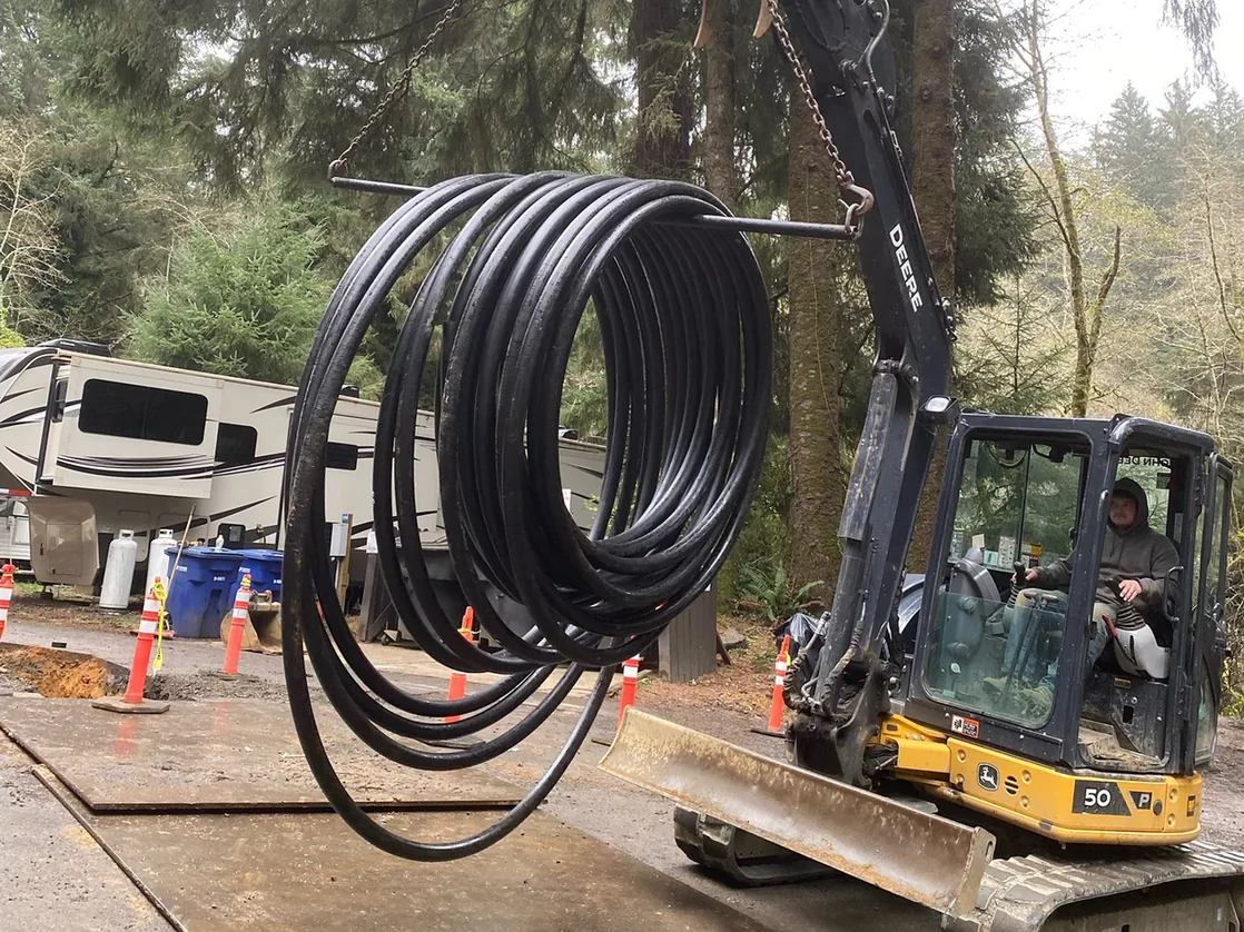 Compact excavator lifting a coil of black water pipe, underground utilities